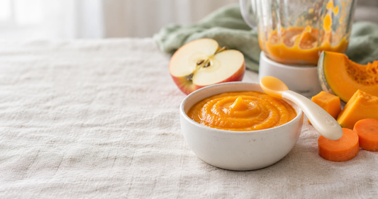 A small bowl of pumpkin puree with a soft baby spoon, steamed carrot and apple