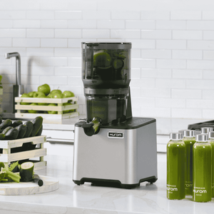 Hurom CP504 slow juicer on a kitchen counter with green juice bottles and fresh vegetables